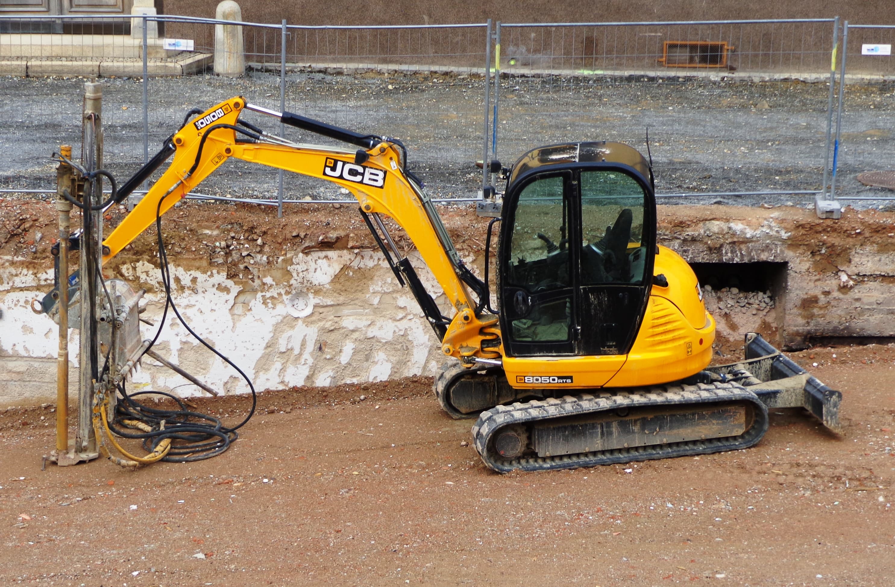 Mini excavator parked beside a hydraulic breaker attachment on a dug-out foundation